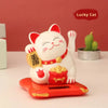 A white ceramic cat with a red nose and waving arm sits on an orange solar-powered platform.
