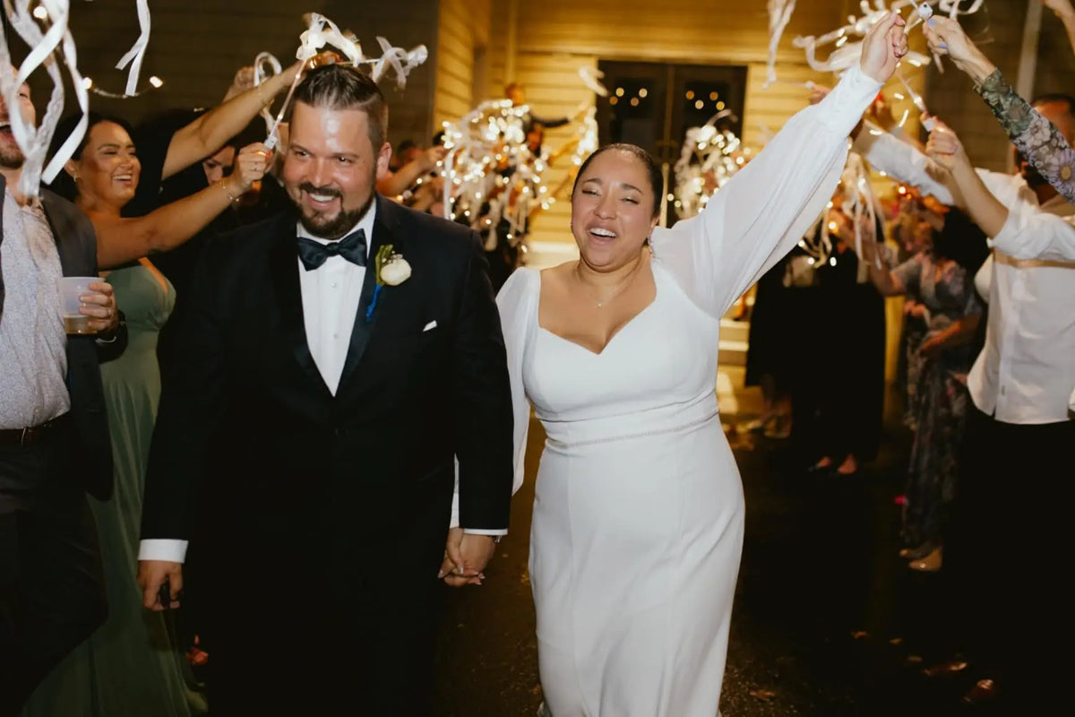 A bride and groom are joyfully waving LED glow wands with ribbons and bells during a wedding celebration.