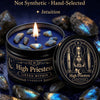 A dark candle jar labeled High Priestess with blue crystal stones and a tarot card on a dark surface.
