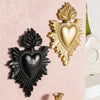 Two heart-shaped wall decorations made of resin, one black and one gold, mounted on a pink wall.