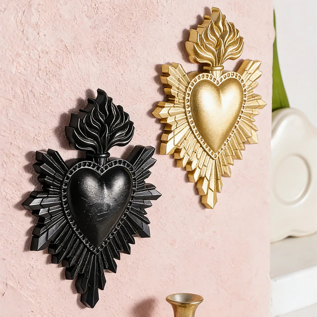 Two heart-shaped wall decorations made of resin, one black and one gold, mounted on a pink wall.