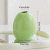 A smooth, light green ceramic mini vase with a rounded shape is shown on a white surface.