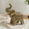 A golden resin elephant sculpture with a curved trunk and intricate detailing, resting on a light fabric.