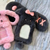 Dunkelgrauer Cartoon-Plush-Fotokarten-Halter mit rosa Akzenten und einem flauschigen rosa Plüschartikel daneben.