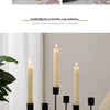 A black iron candle holder with a cream-colored candle on a white table, set in a bright room.