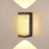 A square, rectangular outdoor wall sconce with a textured gold LED crystal light is mounted on a white wall.