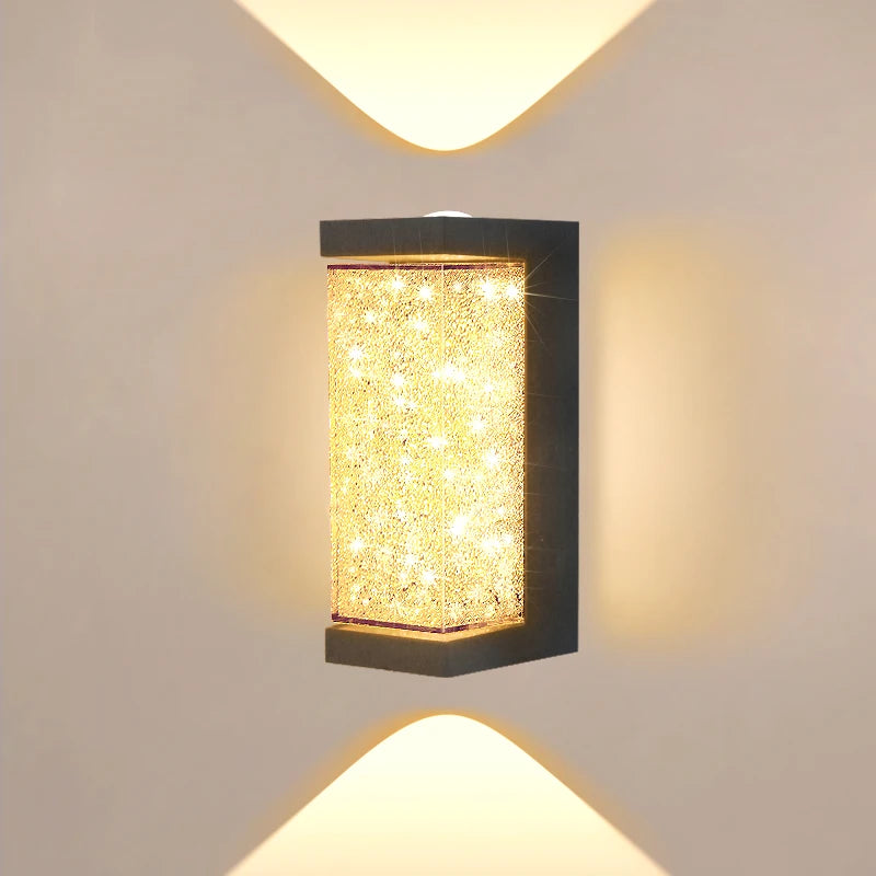 A square, rectangular outdoor wall sconce with a textured gold LED crystal light is mounted on a white wall.