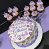A birthday cake decorated with purple and pink flowers, surrounded by small cupcakes topped with matching butterfly decoratio