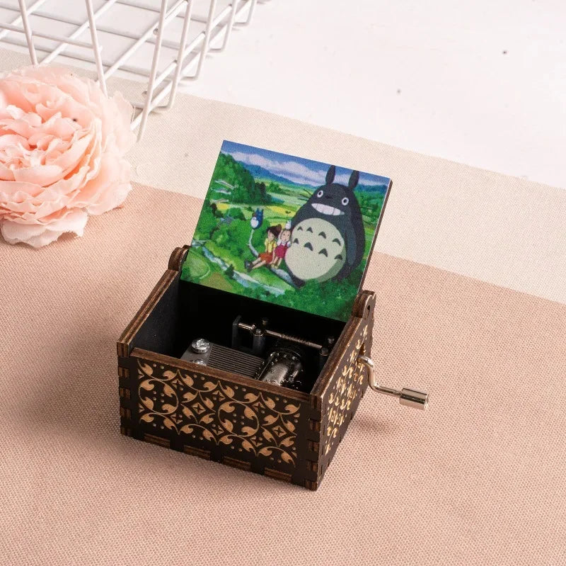 A hand-cranked wooden music box featuring a Totoro design, set against a light beige background.