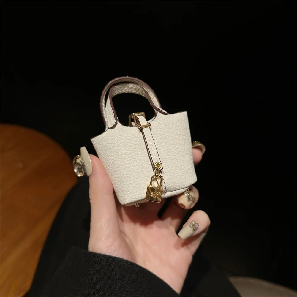 A hand holds a small, off-white mini handbag with a gold wrist strap against a dark background.