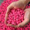 A hand holds a pile of bright pink miniature resin flamingo duck figurines for crafts and cake toppers.