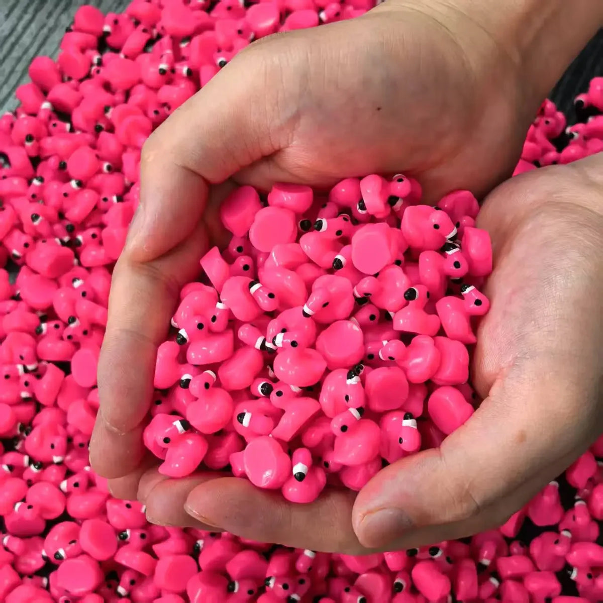 A hand holds a pile of bright pink miniature resin flamingo duck figurines for crafts and cake toppers.