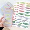 A hand holds a pink smartphone next to a stack of colorful Bible verse stickers for journals and planners.