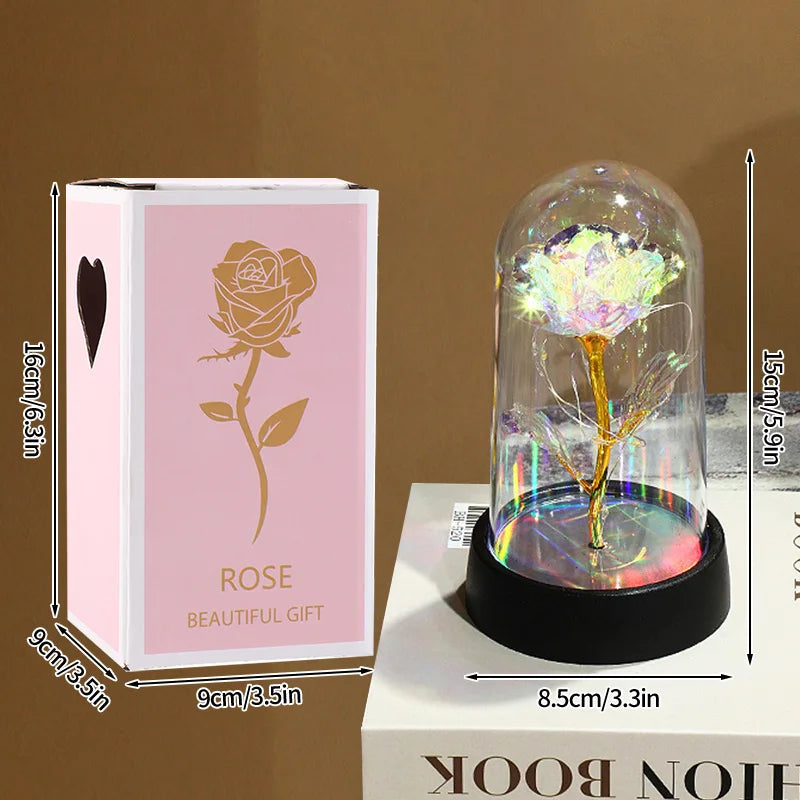 A pink box containing an eternal rose in a glass dome sits next to a white book.