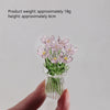 A hand holds a small bouquet of pink glass flowers in a clear glass vase.