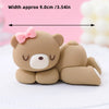 A cute, round, light brown cartoon elephant cake topper with pink ears and a bow, shown on a white surface.