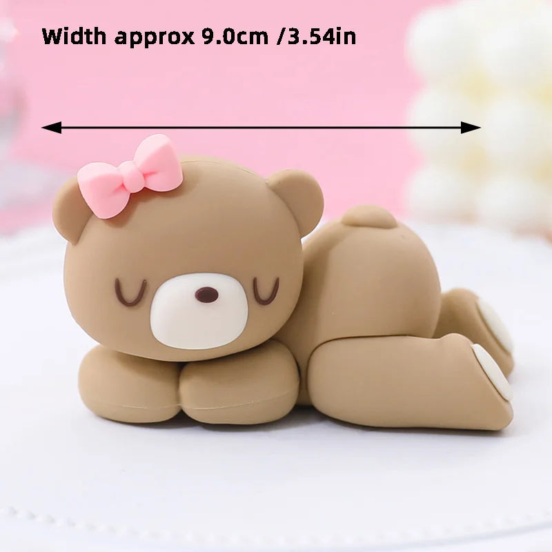 A cute, round, light brown cartoon elephant cake topper with pink ears and a bow, shown on a white surface.