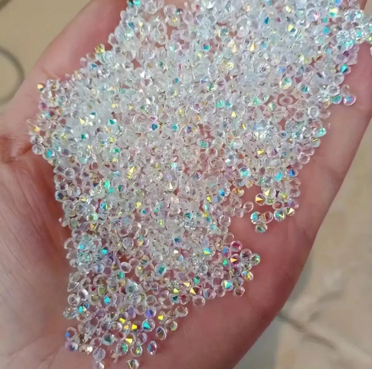 A hand holds a scattering of iridescent nail rhinestones for DIY art.