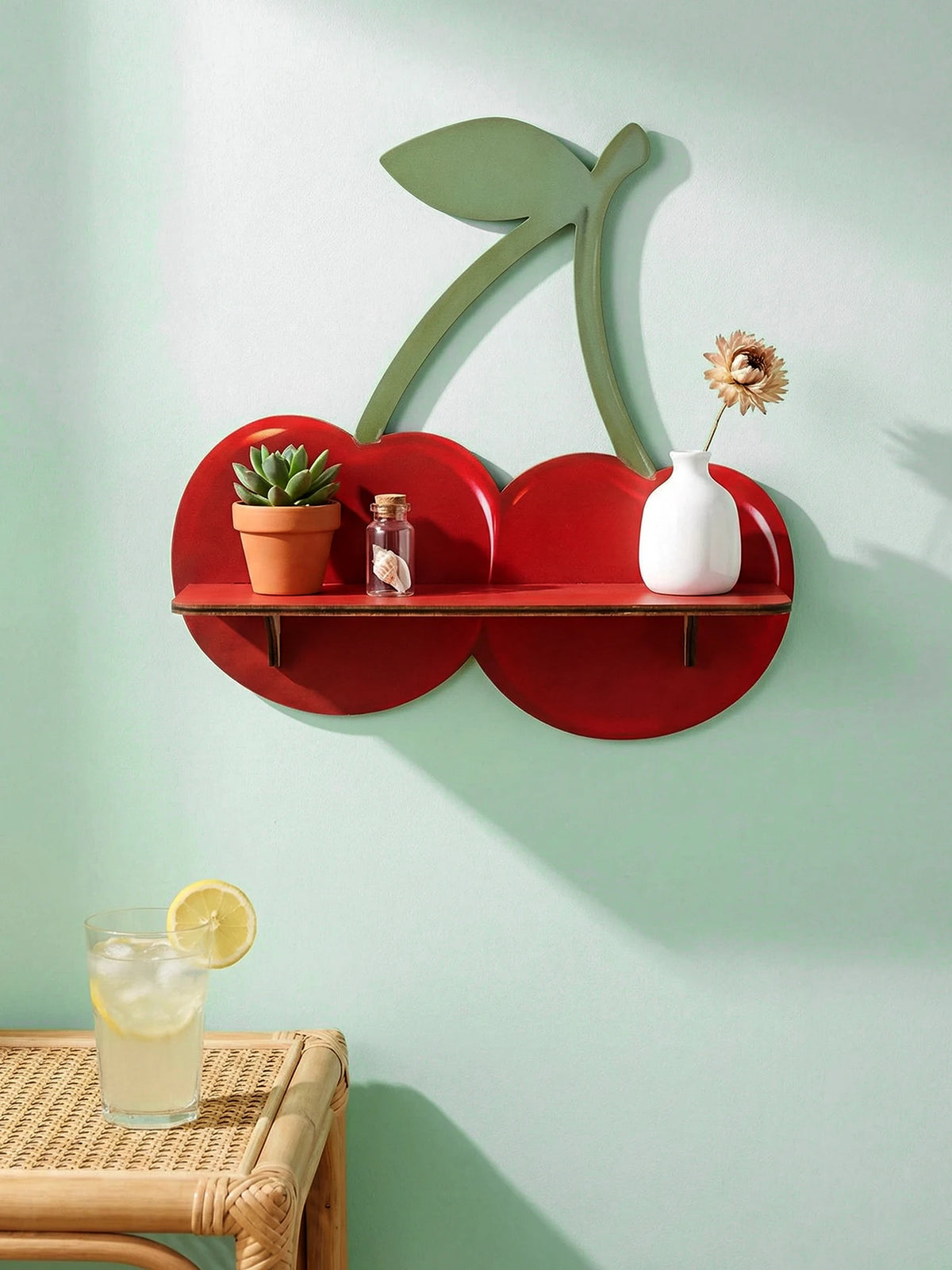 A wooden shelf shaped like a cherry, mounted on a light green wall, holding potted plants and white ceramic items.