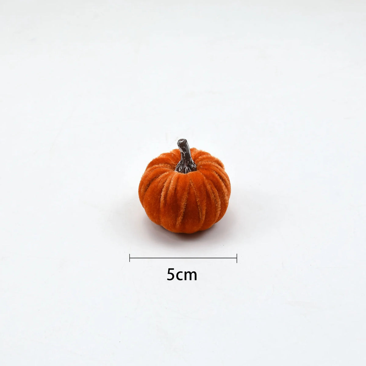 A small, round, orange velvet pumpkin decoration with a stem, shown against a white background.
