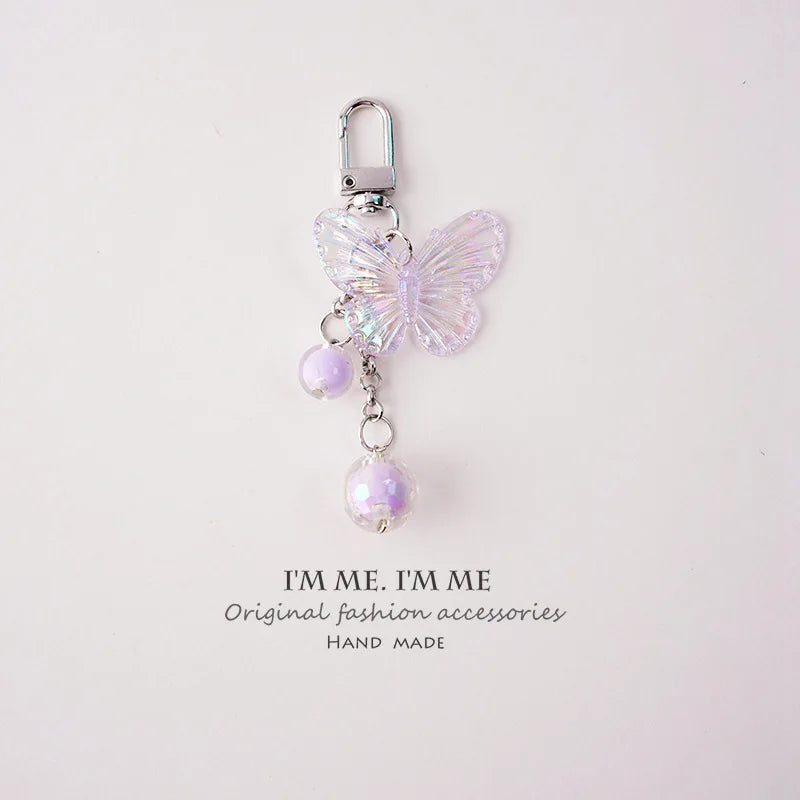 A silver-hooked butterfly pendant keychain set featuring pink iridescent wings and purple beads.