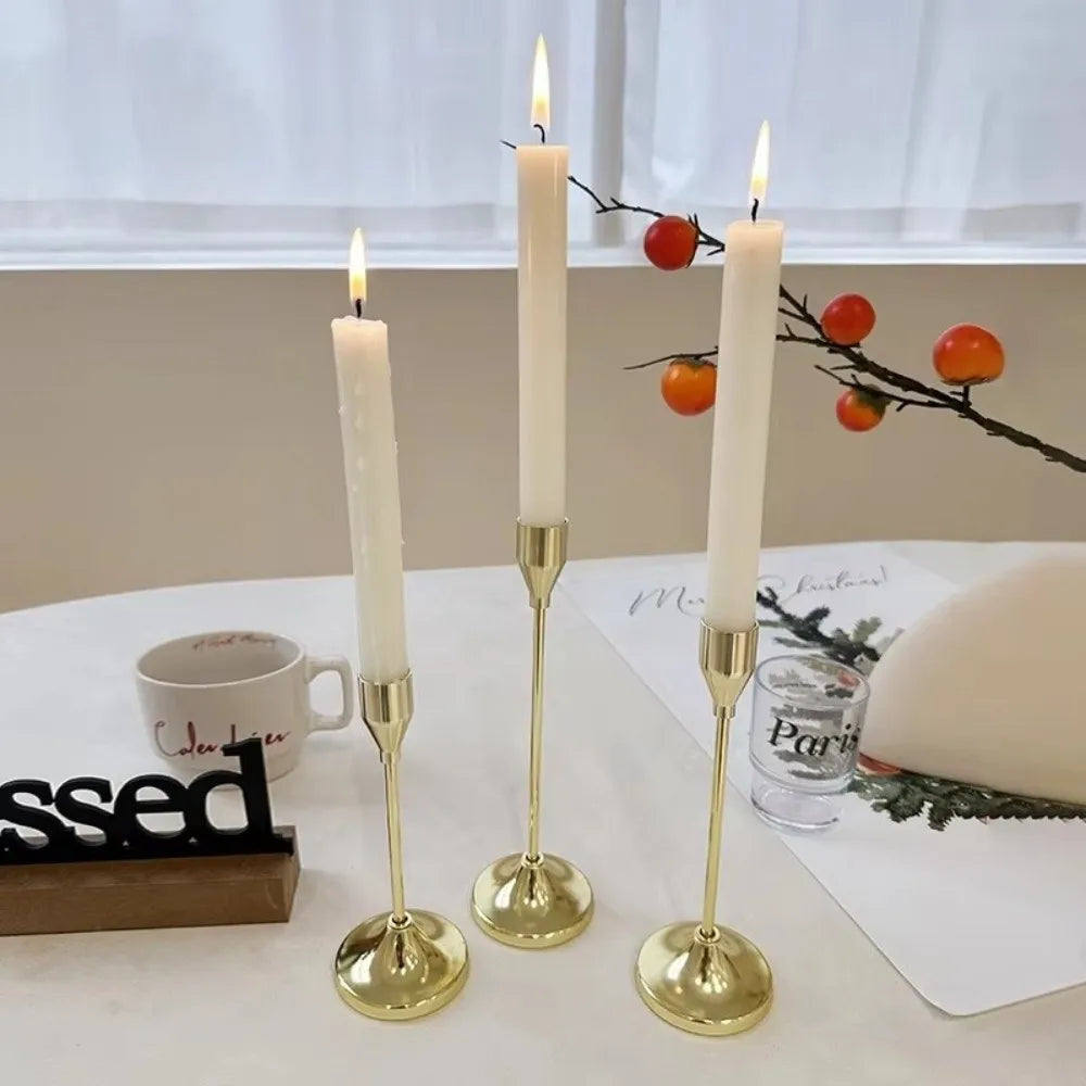 A set of three gold-toned candle holders with white taper candles and orange berries on a white table.