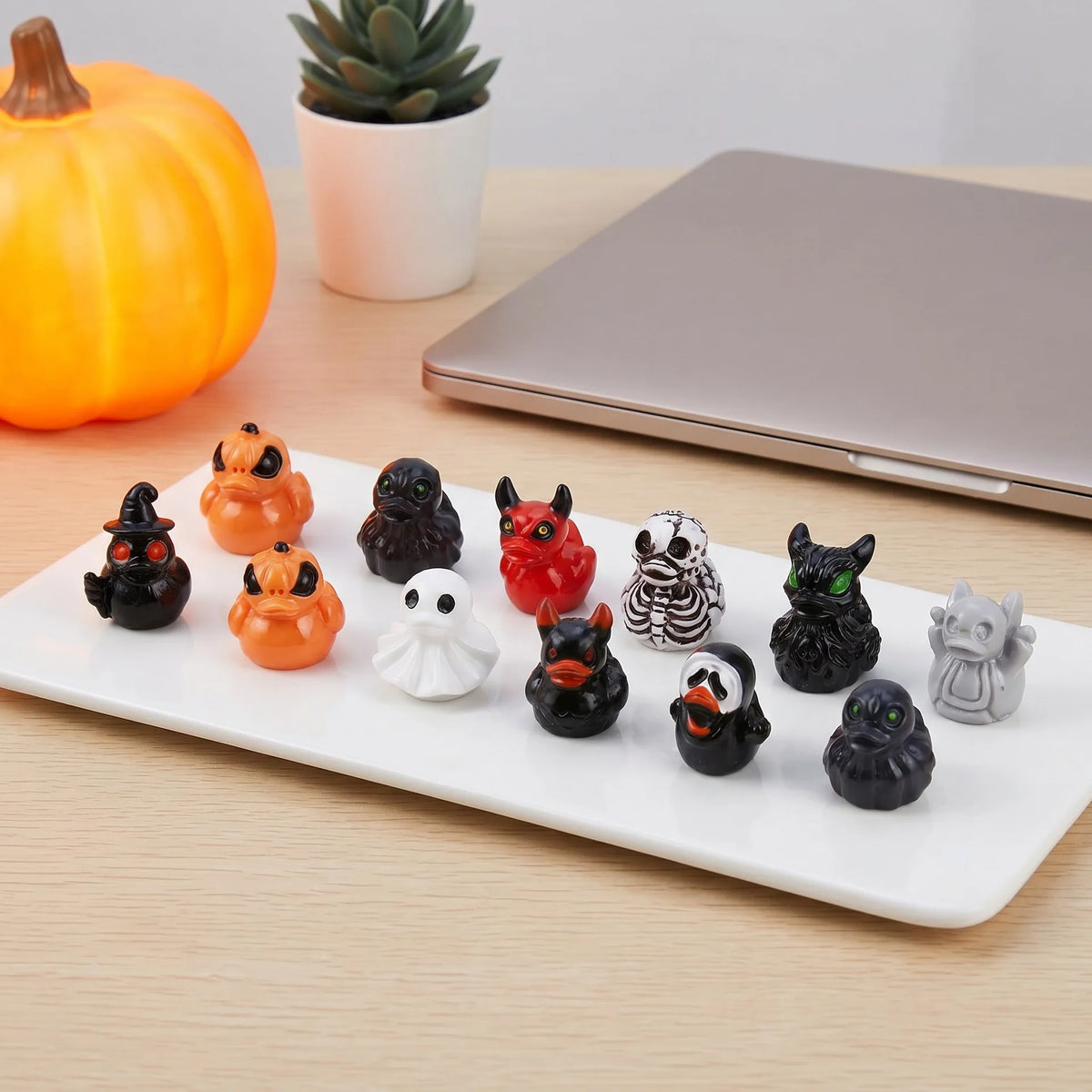 A white rectangular platter holds a set of twelve mini resin Halloween duck figurines in various colors and shapes.