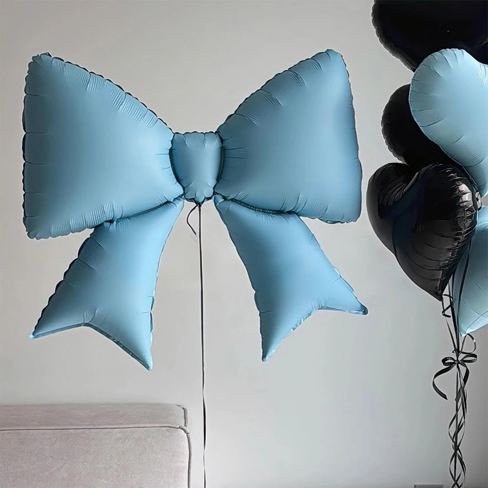 Light blue bow-shaped foil balloon decoration hanging against a white wall.