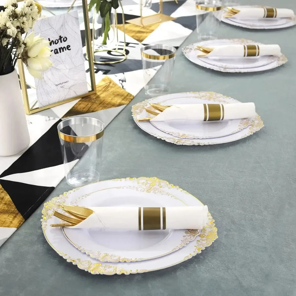 Elegant white and gold disposable dinnerware set with cutlery arranged on a gray table.
