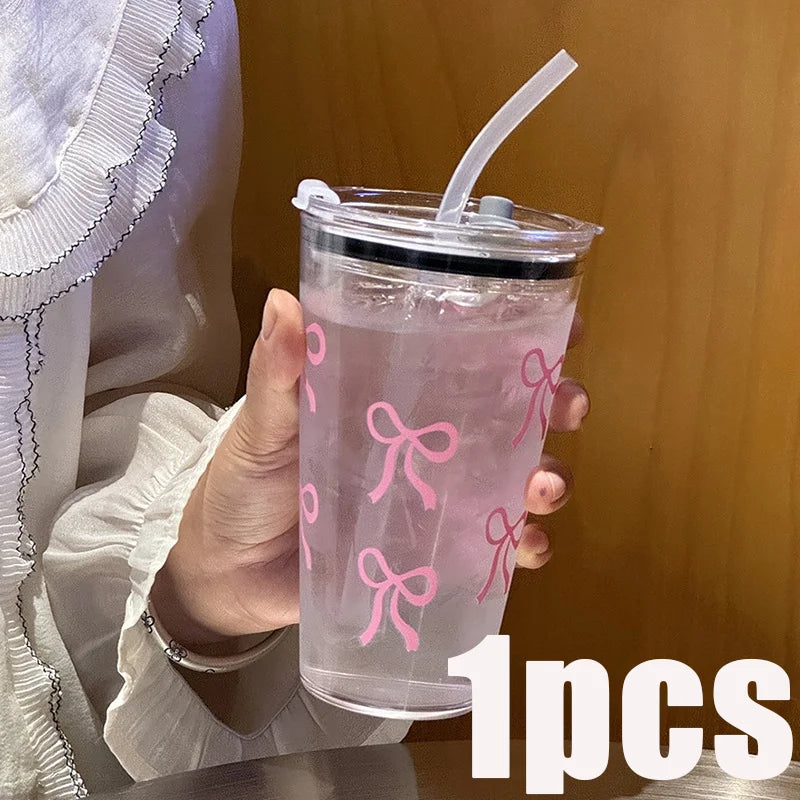 A hand holds a clear pink plastic cup with a lid and straw, decorated with pink bow patterns.