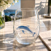 A clear glass wine glass filled with water features a sculpted blue-ringed octopus design on a marble surface.