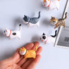 A hand holds several 3D cartoon cat refrigerator magnets in various colors and poses.