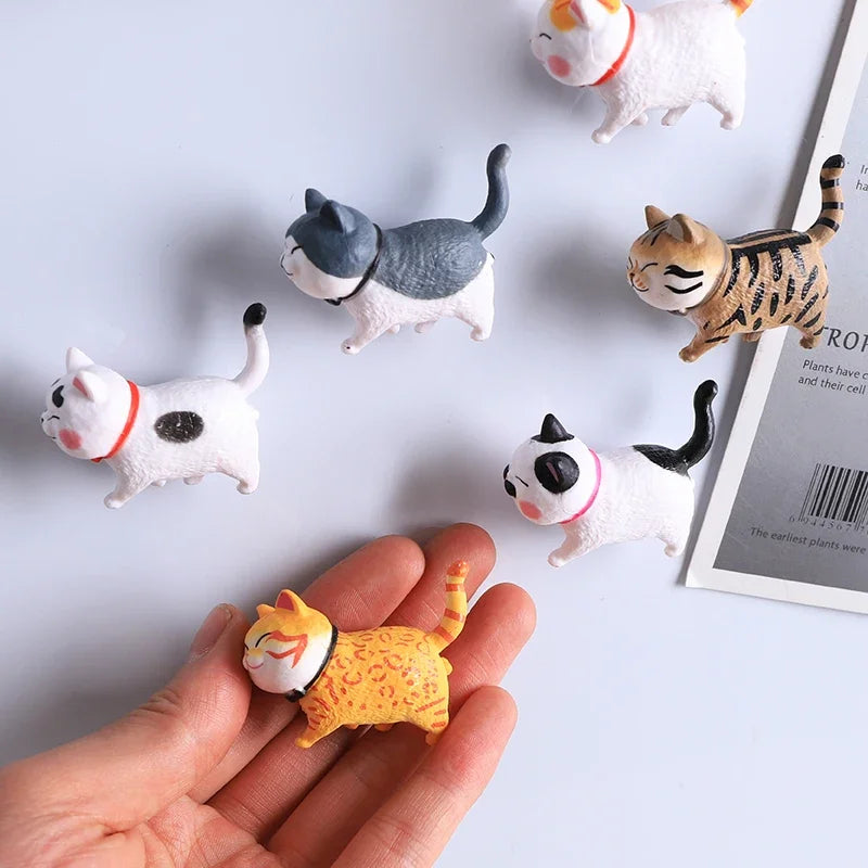 A hand holds several 3D cartoon cat refrigerator magnets in various colors and poses.
