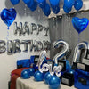 Blue and silver balloon decor featuring happy birthday letters, heart balloons, and foil numbers on a table.