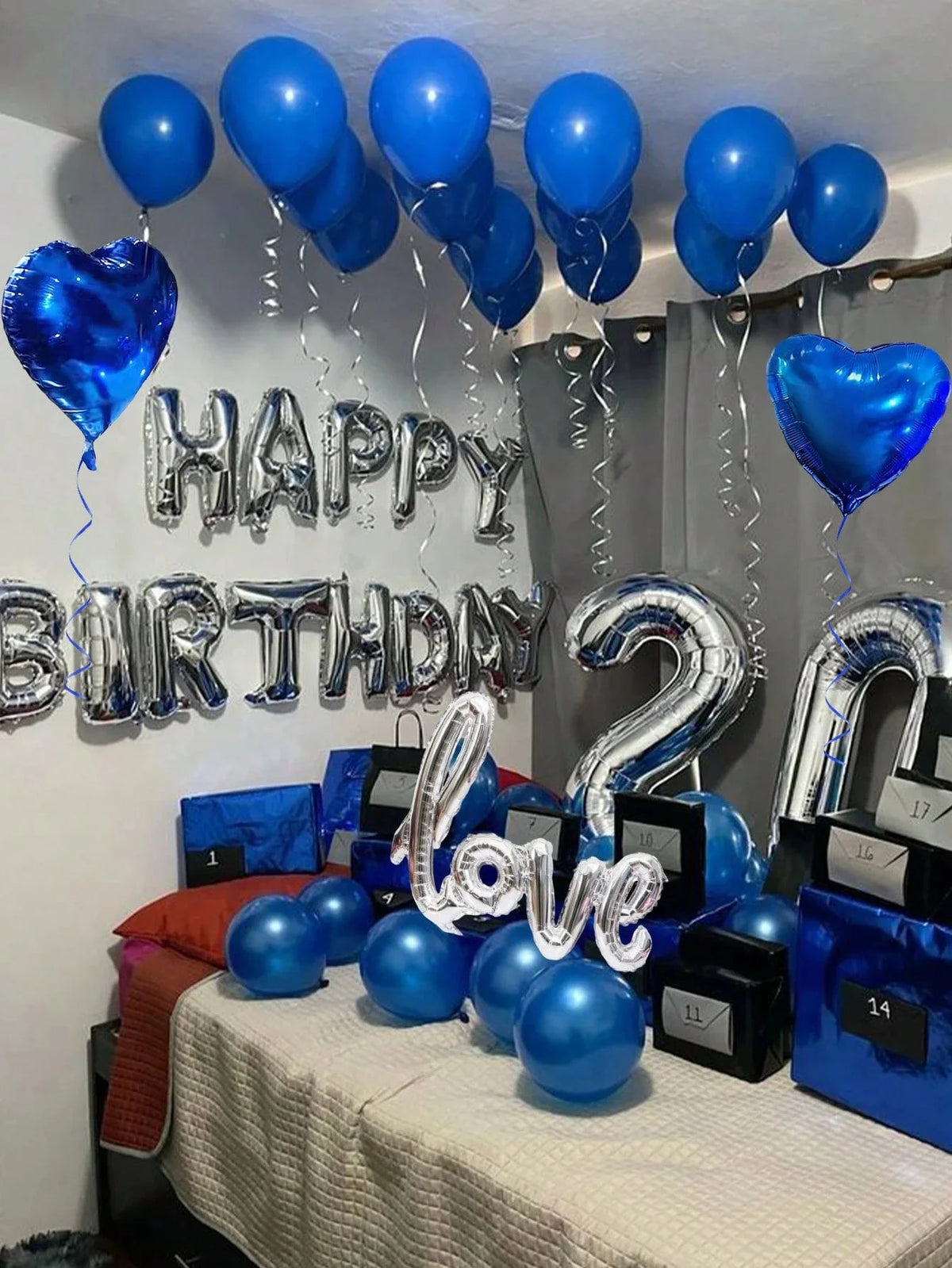 Blue and silver balloon decor featuring happy birthday letters, heart balloons, and foil numbers on a table.