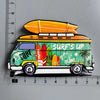 A colorful magnet shaped like a yellow van with a surfboard on the roof and tropical foliage.