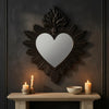 A dark wall decor featuring an ornate, heart-shaped mirror with a textured frame and lit candles below.