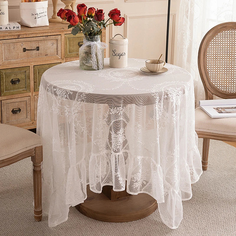 Elegant white floral lace tablecloth covering a round table set with red roses and sugar