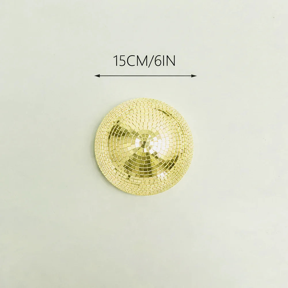 A round, gold-colored disco ball with a textured surface is shown against a light background.