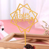 A gold acrylic happy birthday topper with a geometric shape and text on a wooden background.