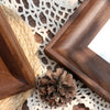 A dark brown wooden photo frame is placed on a beige crocheted mat next to a pinecone.