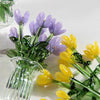 A bouquet of hand-blown glass flowers featuring purple and yellow tulips in a clear glass vase.