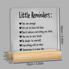 A white acrylic desk plaque with black text featuring little reminders like You are enough and Everything will be okay.