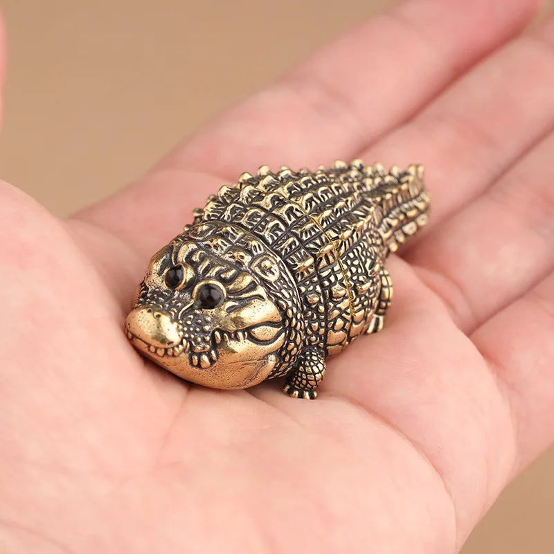 Antique brass crocodile figurine resting on a person's palm.