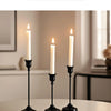 Three elegant black metal candlesticks with white candles on a table for home decor