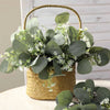 A bundle of artificial eucalyptus stems with small white flowers in a woven basket for home decor
