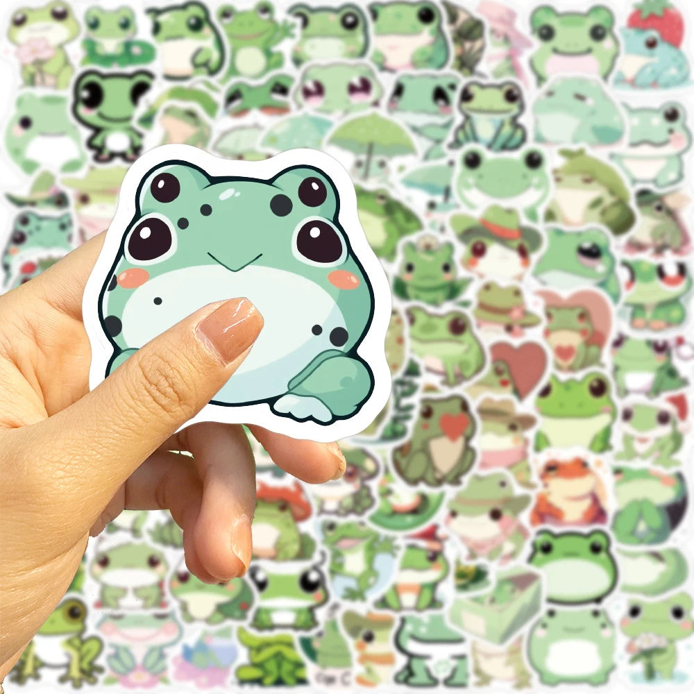 Une main tient une étiquette transparente avec un design de grenouille esthétique parmi d'autres autocollants de grenouilles.