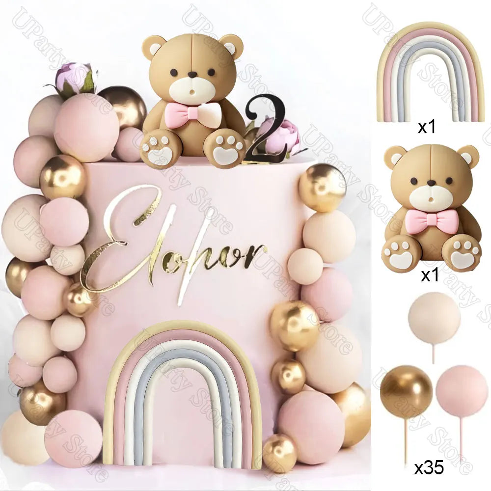 A set of boho rainbow cake toppers featuring a teddy bear, pink balls, and gold accents.