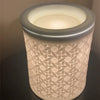 A cylindrical white wax warmer with a textured pattern and a frosted glass light bulb inside.