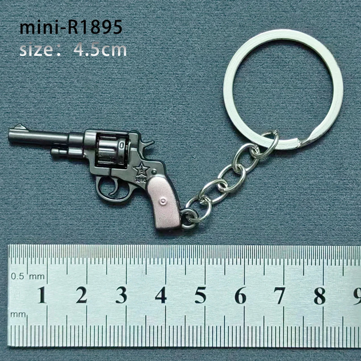 A miniature alloy gun model keychain with a silver finish and a silver ring, measured against a ruler.